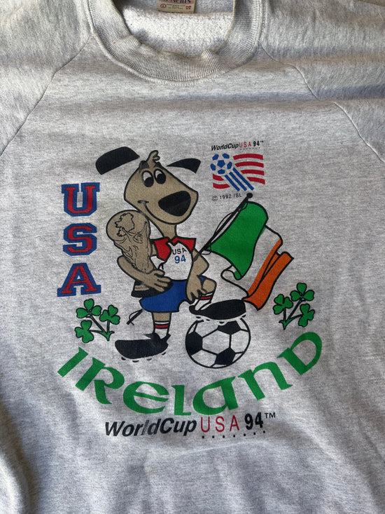 Retro sports sweatshirt with USA and Ireland flags, soccer ball, and cartoon mascot.