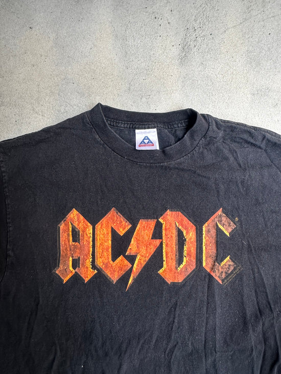 Black AC/DC band t-shirt with distressed orange logo, laid flat on a textured surface.