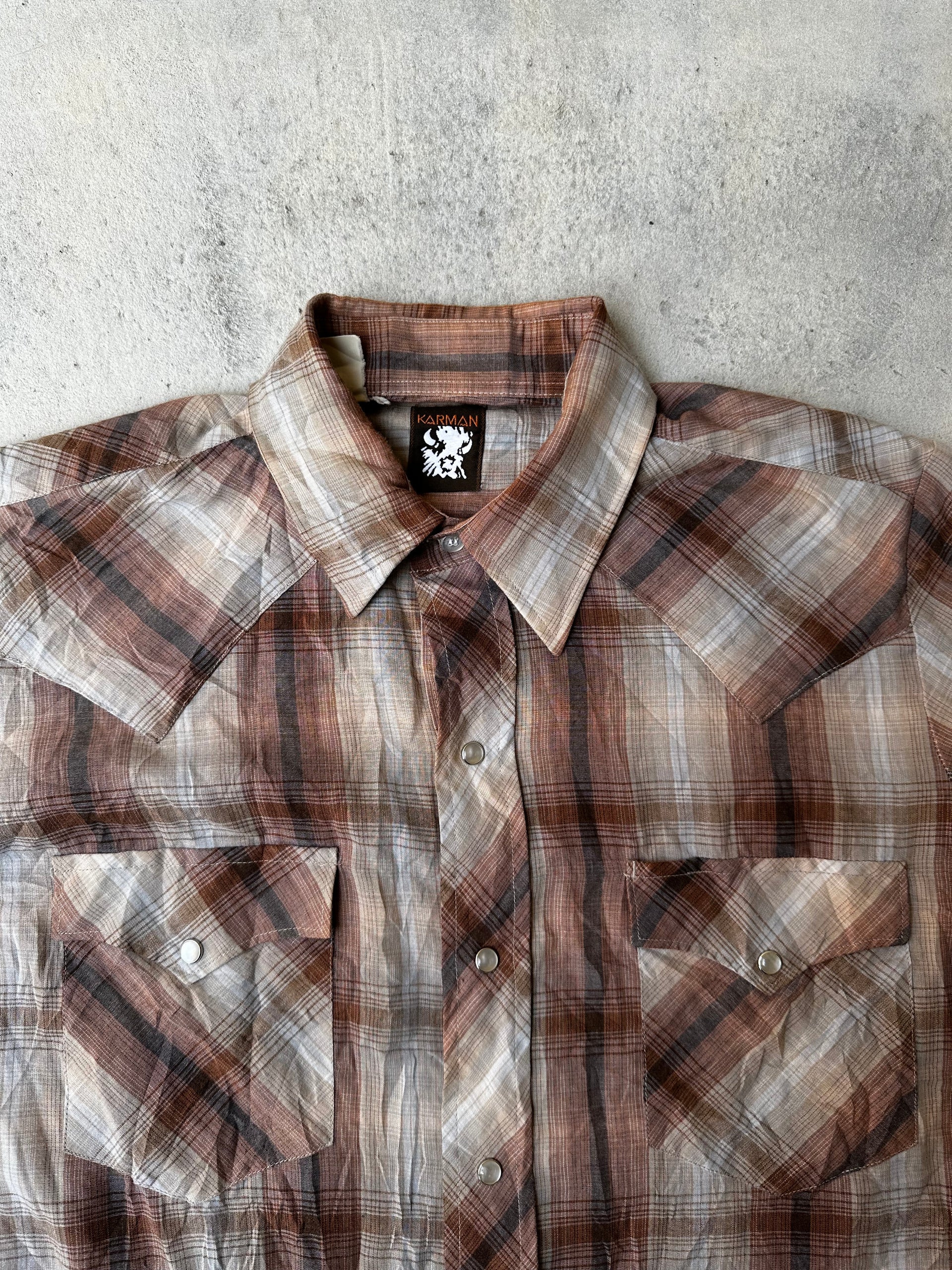 Close-up of western pearl snap closure on rugged plaid shirt.
